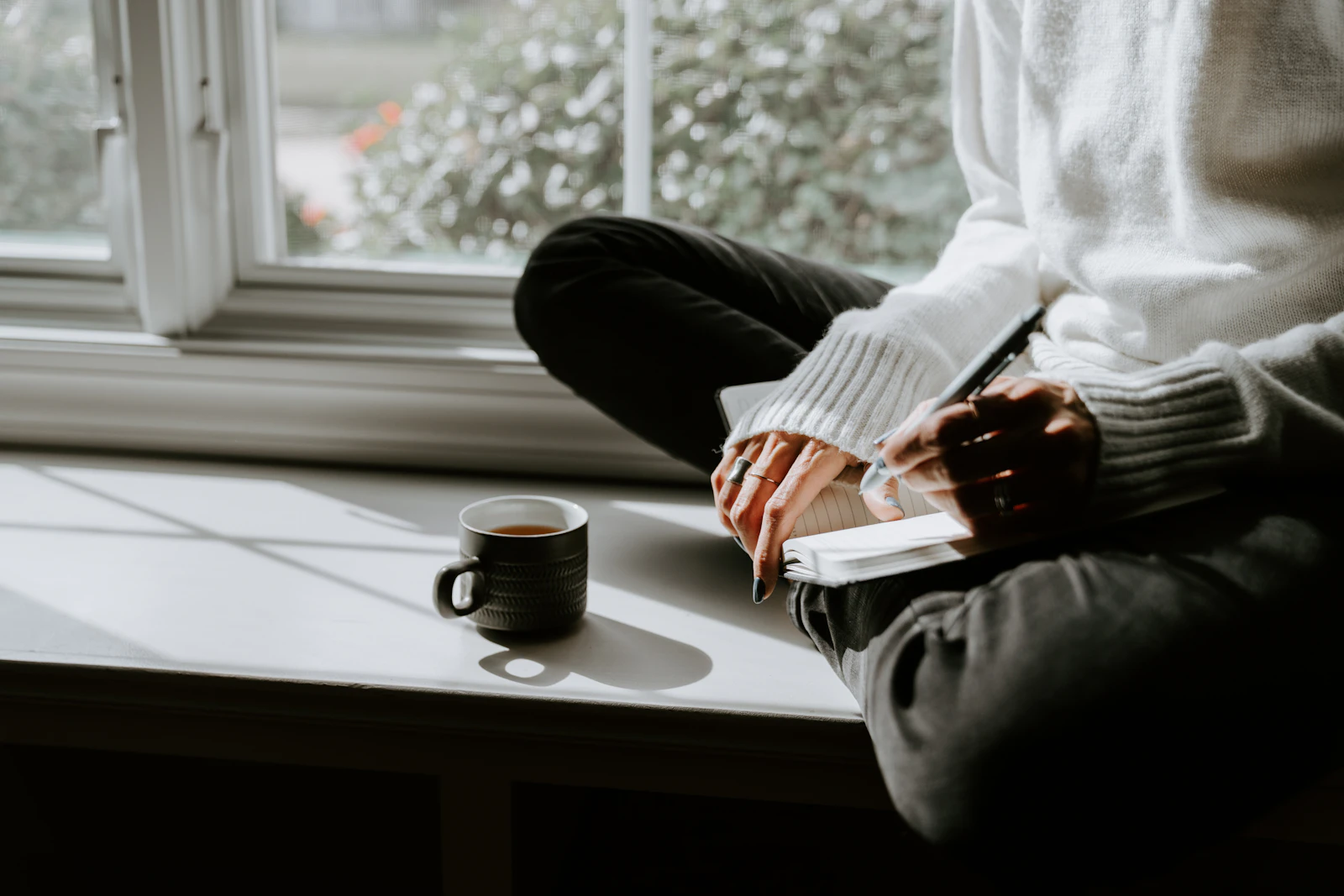 Personne assise avec une tasse de café à la fenêtre - ambiance coaching de vie matinal.
